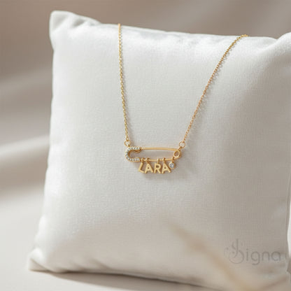 Signa™ Custom Gold Safety Pin Necklace featuring pave diamond accents on the pin head, two personalized initials, and a dangling heart charm. A dainty personalized birthday gift for her shown on a model.