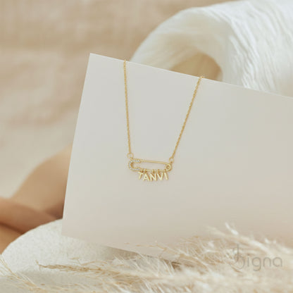Signa™ Custom Gold Safety Pin Necklace featuring pave diamond accents on the pin head, two personalized initials, and a dangling heart charm. A dainty personalized birthday gift for her shown on a model.