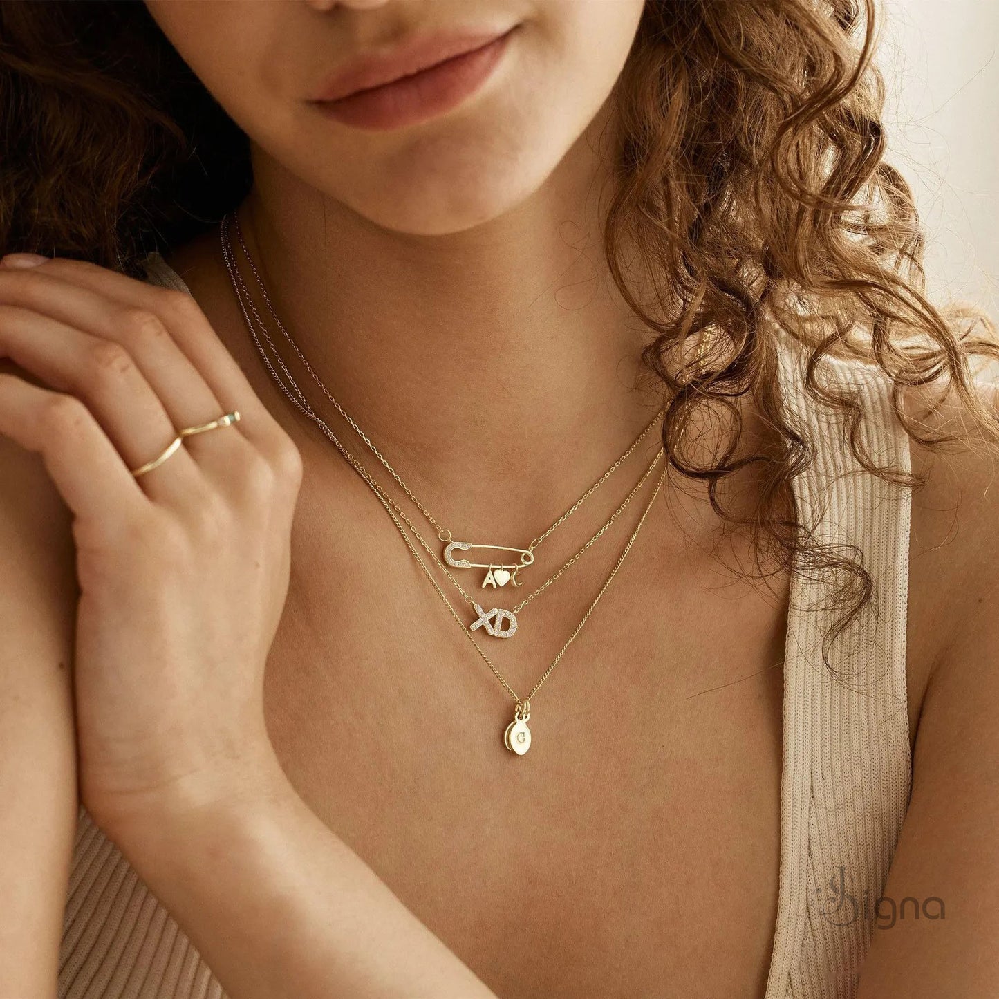 signa™ custom gold safety pin necklace featuring pave diamond accents on the pin head, two personalized initials, and a dangling heart charm. a dainty personalized birthday gift for her shown on a model.