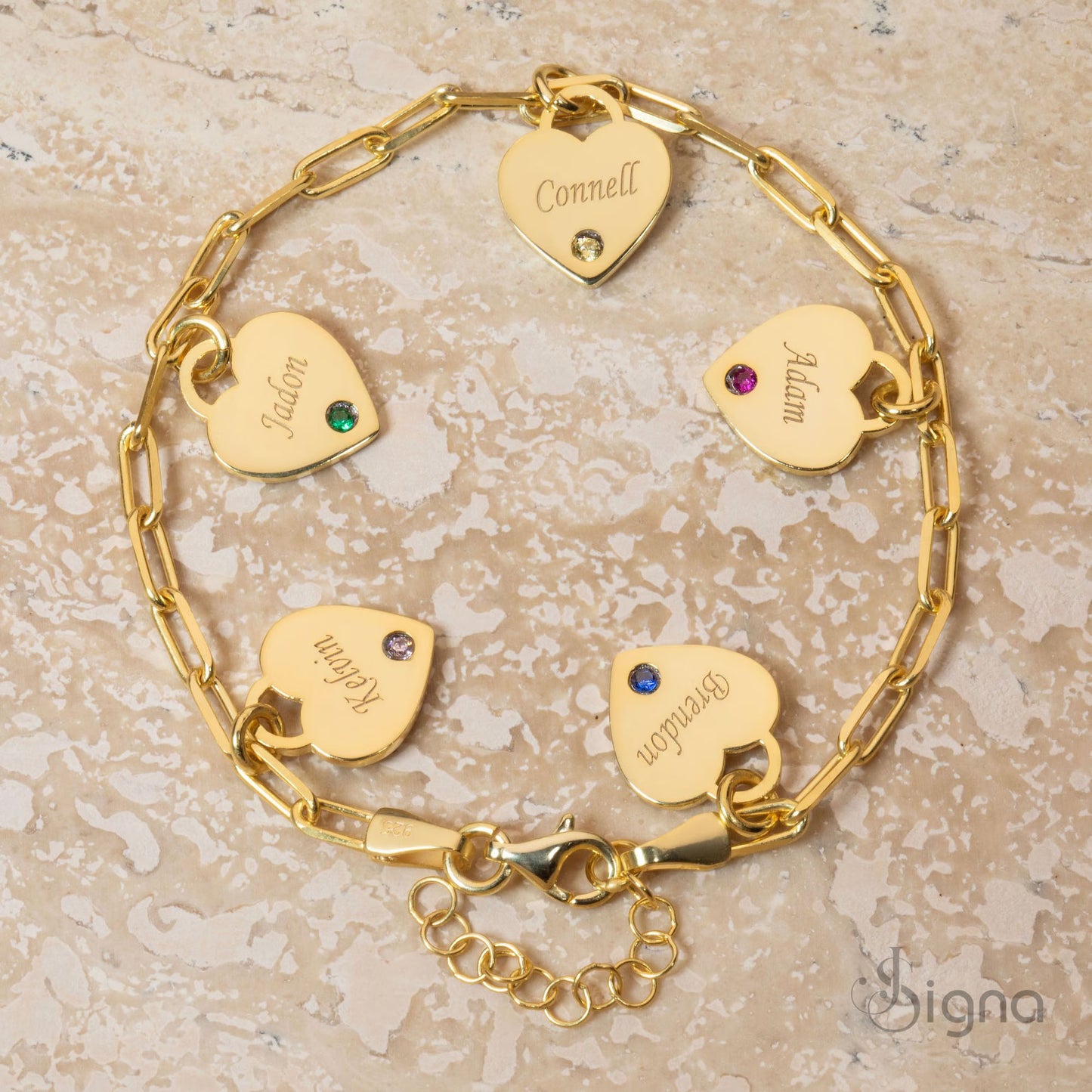 gold bracelet with heart-shaped name tags on a textured beige surface