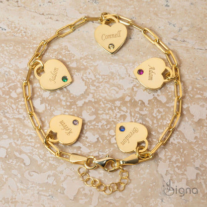 Gold bracelet with heart-shaped name tags on a textured beige surface