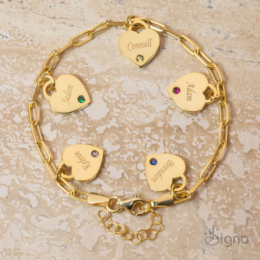 Gold bracelet with heart-shaped name tags on a textured beige surface