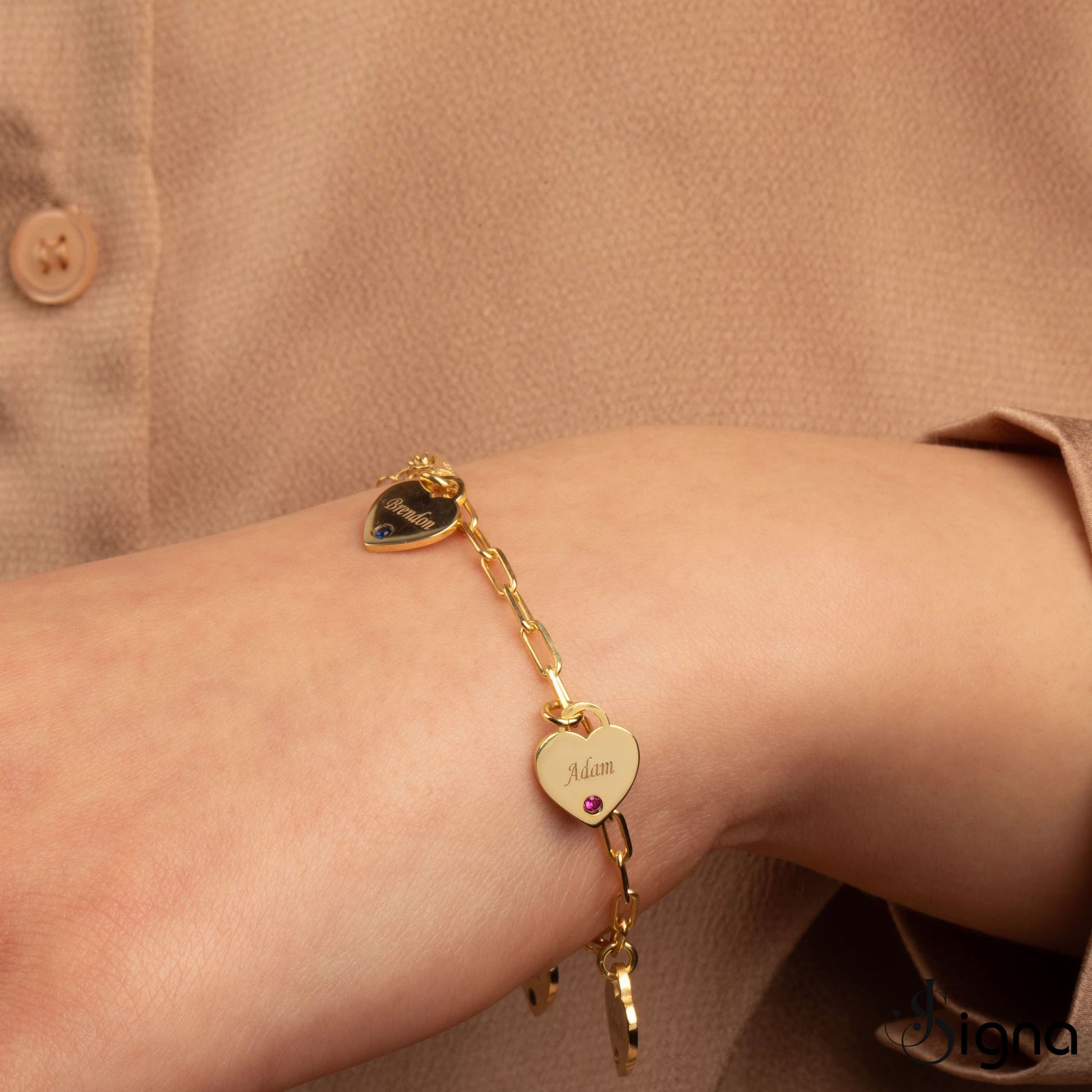 Gold bracelet with heart-shaped charms on a wrist against a beige background