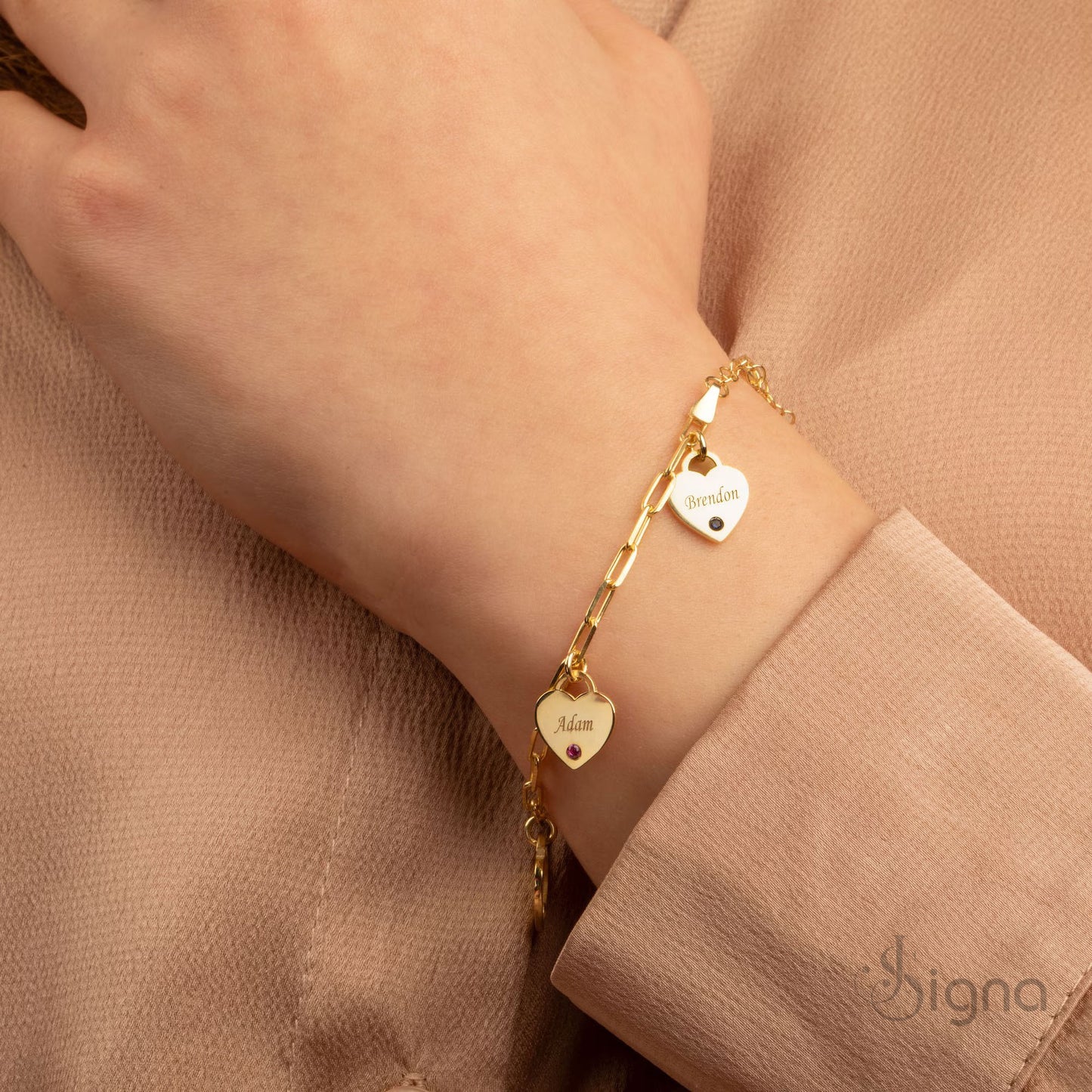 gold bracelet with heart-shaped charms on a wrist against a beige background