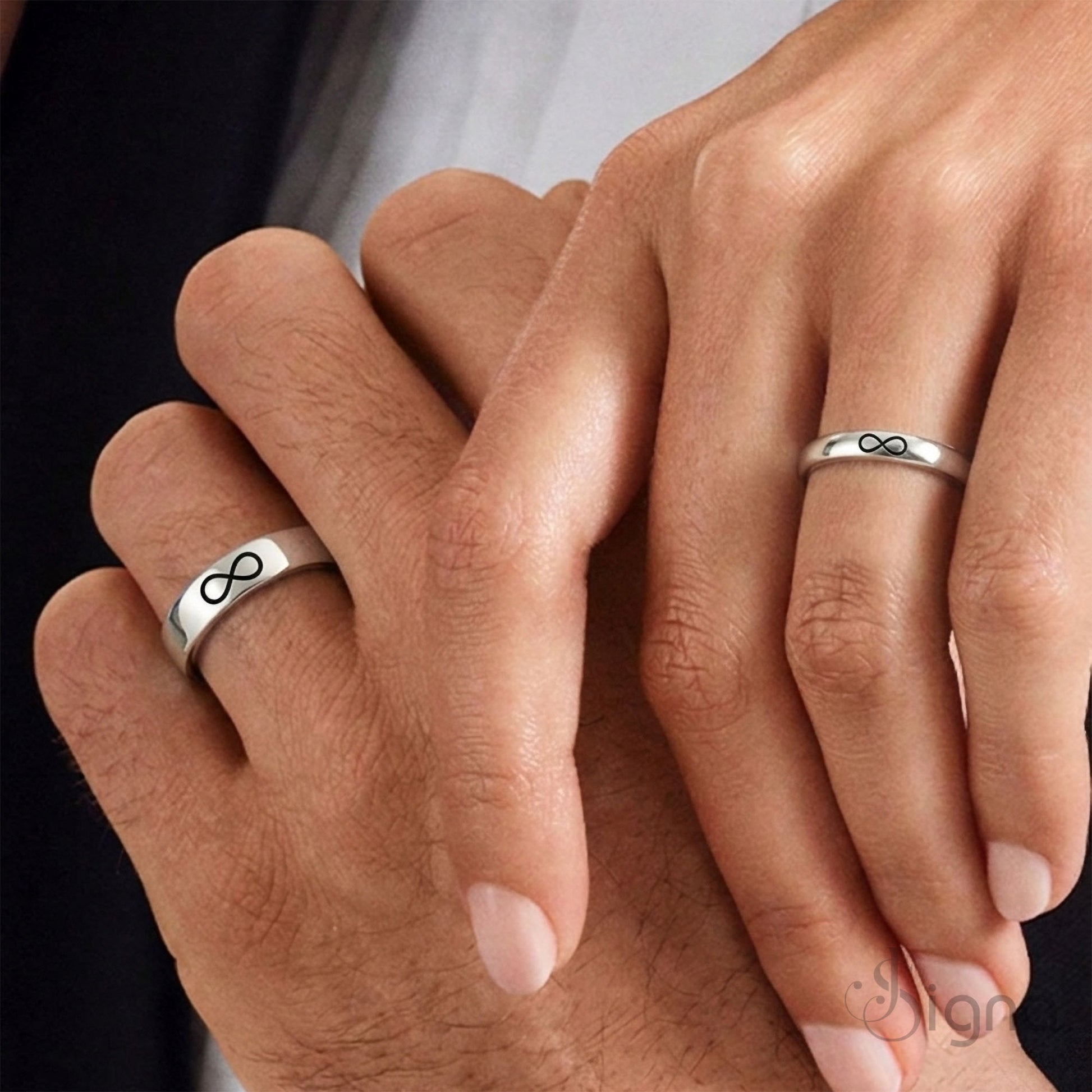 A close-up of a couple's hands joined together, wearing matching Signa™ personalized silver rings with custom secret messages engraved on the inside bands.