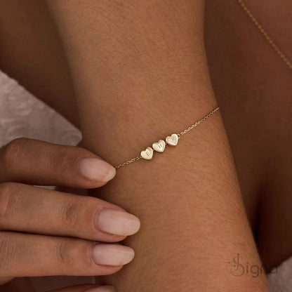 Close up of engraved initial heart charms on gold bracelet