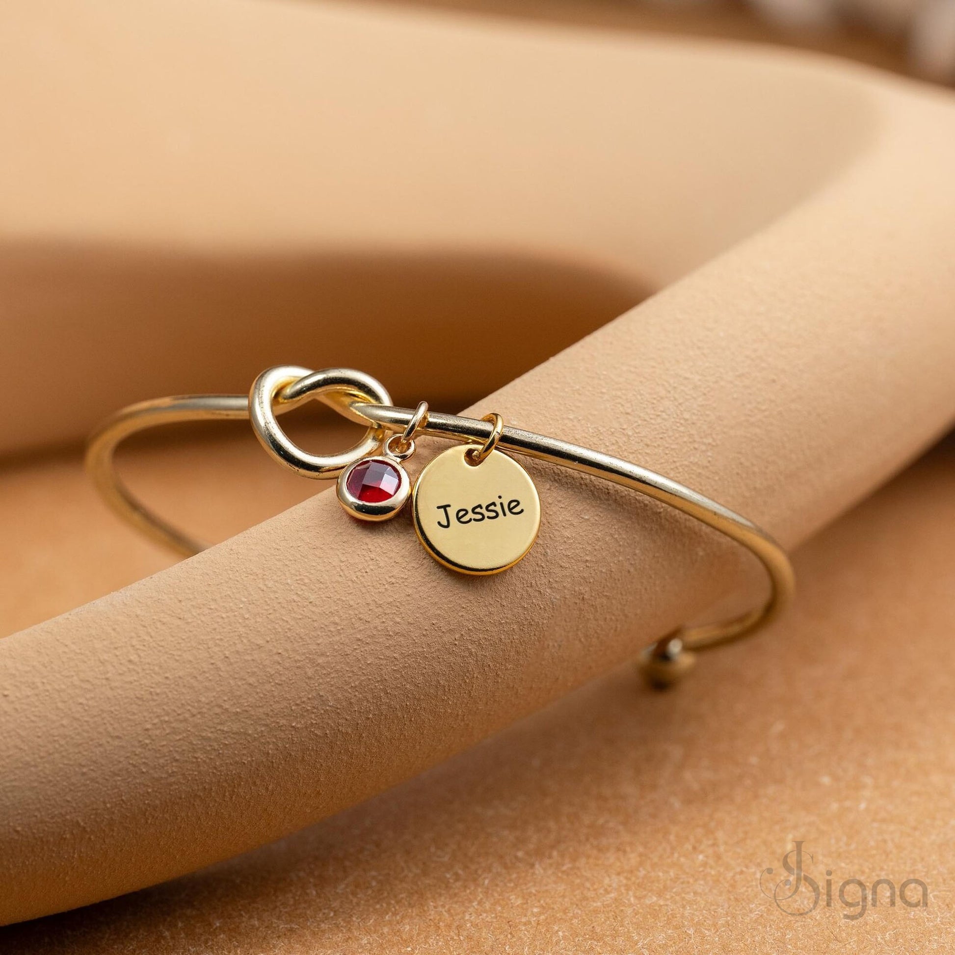 Close-up of engraved name disc and birthstone charm on gold tie-knot bangle